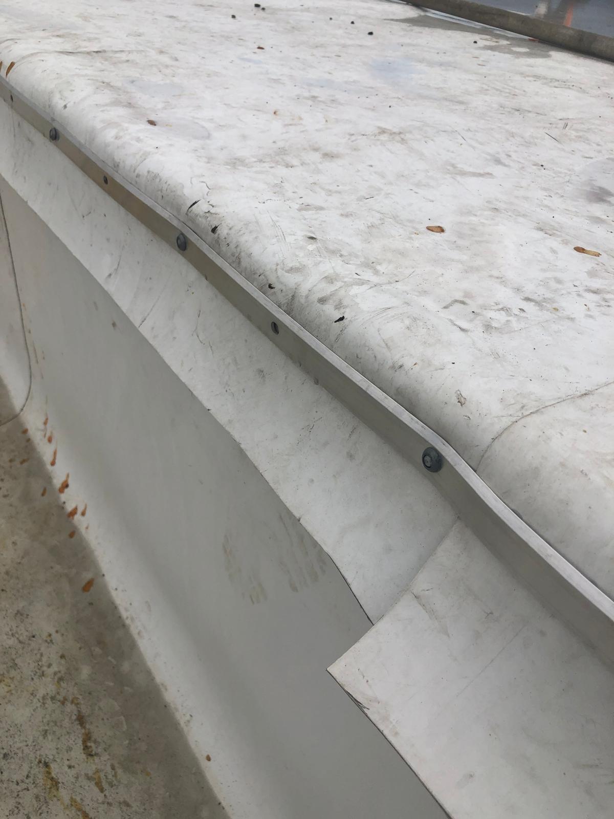 Close-up of a dirty white metal surface with screws and some visible stains, rust, and bent edges.