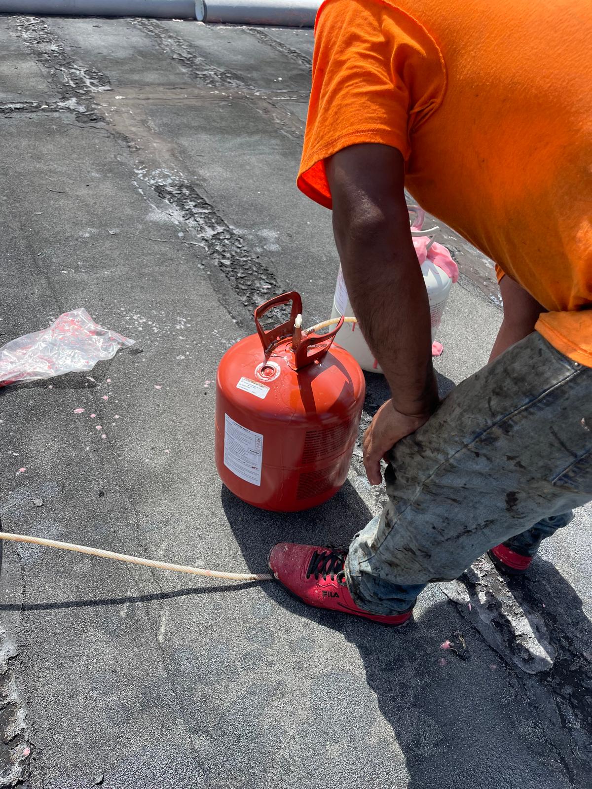 Person in orange shirt and red shoes kneeling next to a red gas canister on a paved surface.