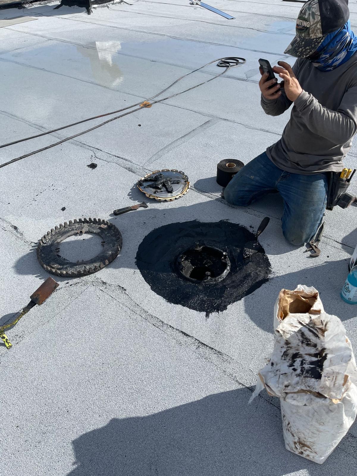 Person kneeling on a roof photographing a removed vent cover and tools during roof repair.