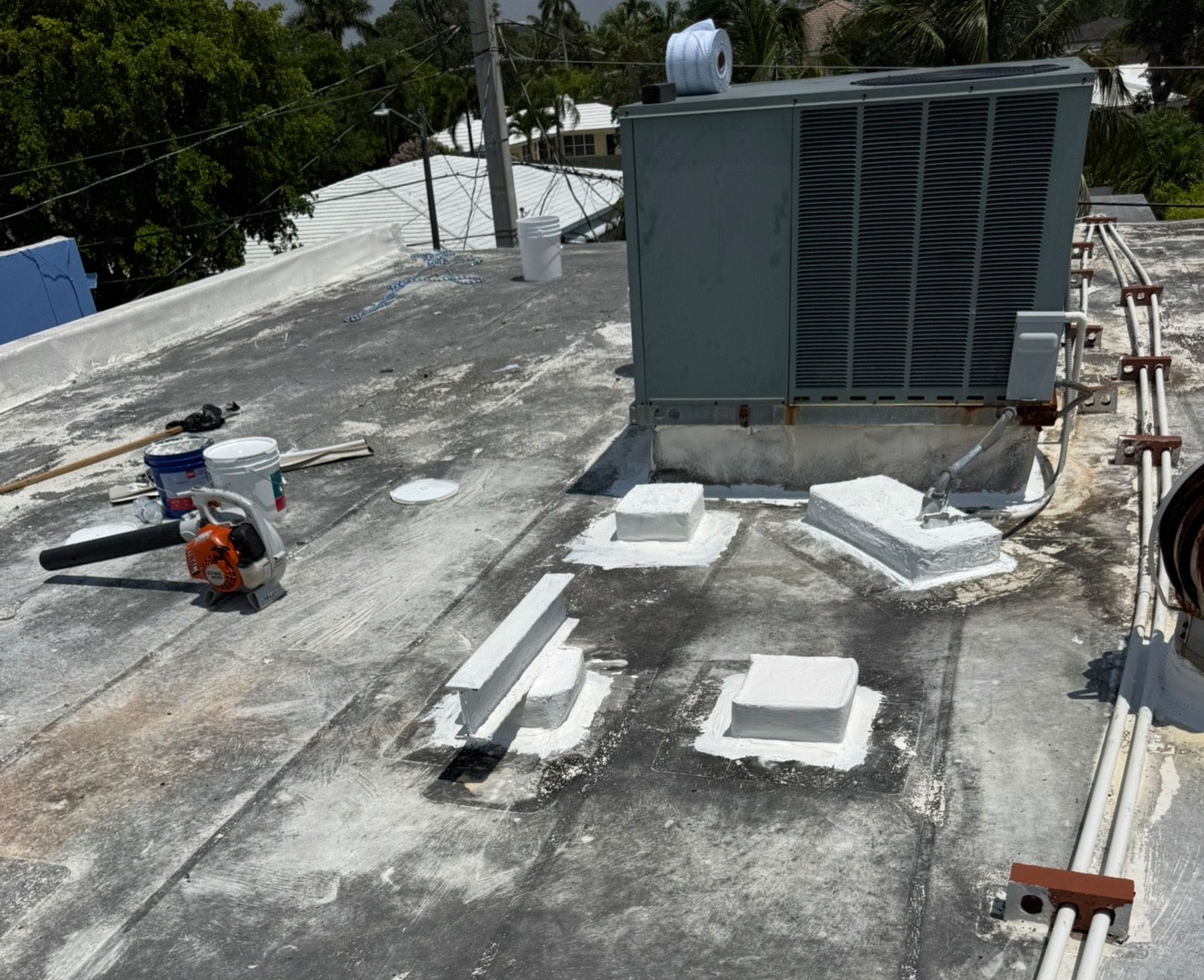 Rooftop with HVAC unit, white sealant patches, tools, and buckets on a sunny day.