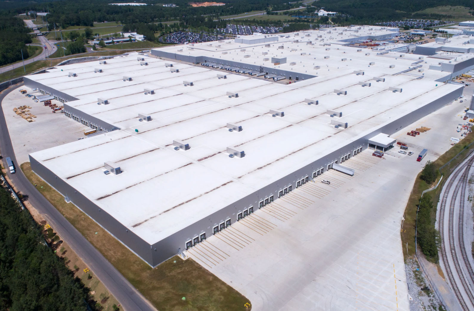 A large industrial warehouse with loading docks, surrounded by roads, trees, and parking lots.